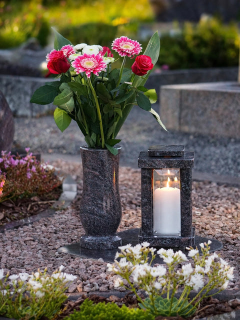 Granit Grabvase mit Blumen und Grablampe mit Kerze auf einem gepflegten Grab an Ostern